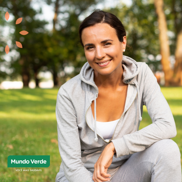 Mulher sorridente em parque, vestindo roupa esportiva, simbolizando saúde, bem-estar e vitalidade feminina.