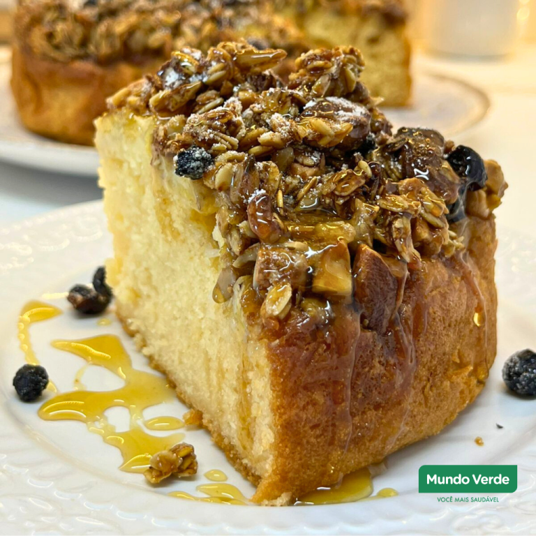 Fatia de cuca de banana com granola sem glúten, macia por dentro e com cobertura crocante, servida em prato branco