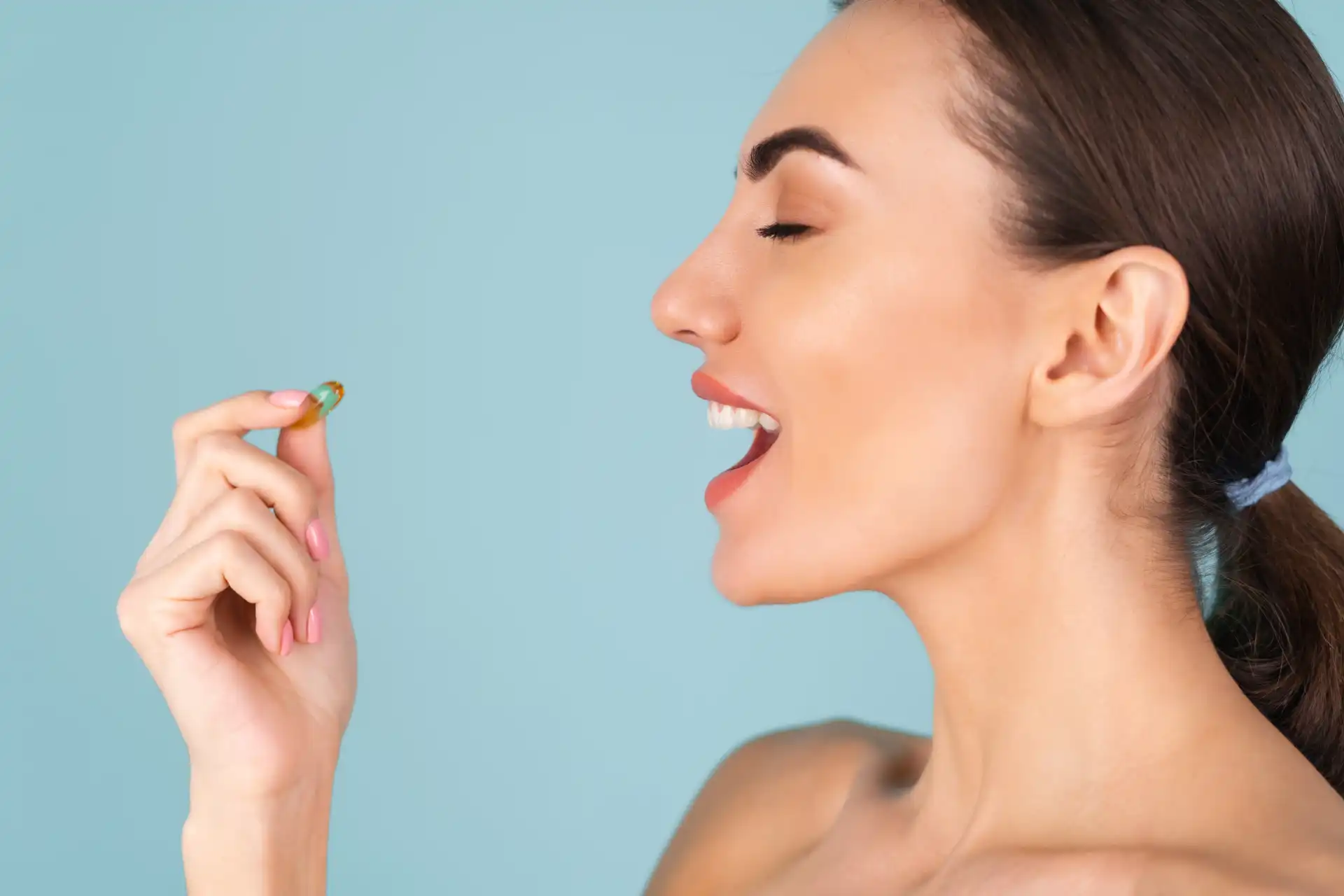 Imagem de uma mulher, em um fundo azul, segurando um comprimido de suplemento alimentar.