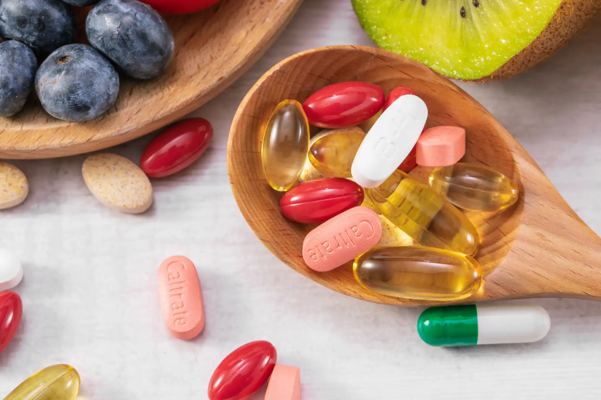 Foto de suplementos alimentares em cápsulas e comprimidos ao lado de frutas como kiwie mirtilos.