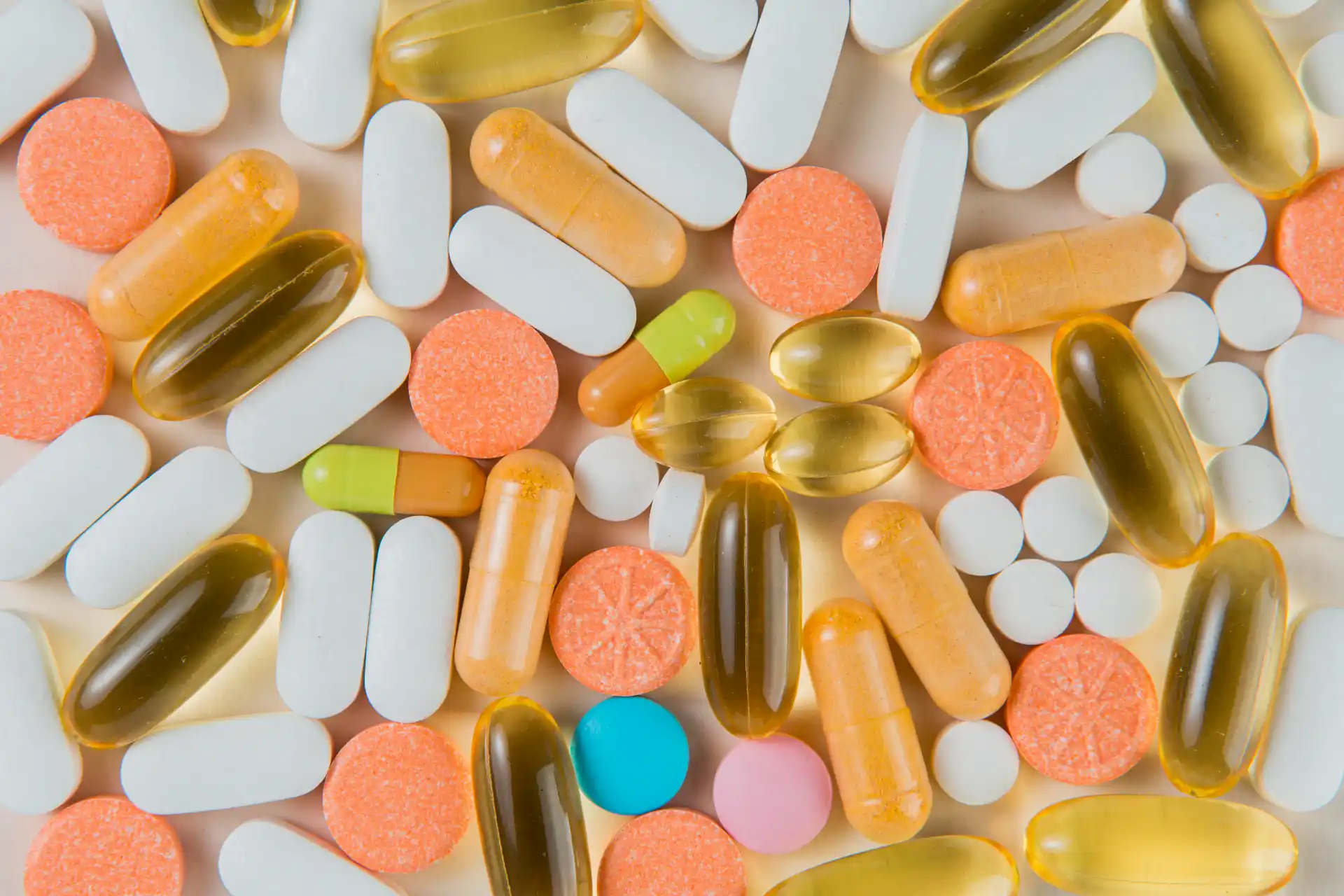Imagem com cápsulas e comprimidos de diferentes cores e tamanhos de suplementos, sobre fundo claro. 